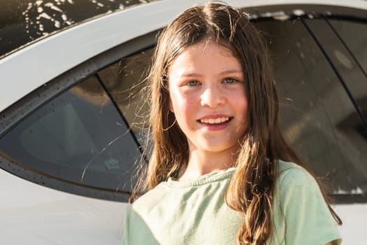 A young girl enthusiastically assists in washing the family's electric car in their suburban driveway.