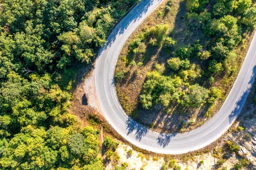 Top view, drone shot of curve of the road  in the pine woods in the mountain