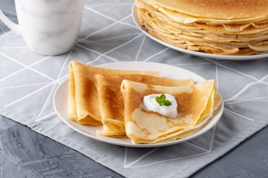 Stack of russian thin pancakes blini with fresh sour cream.