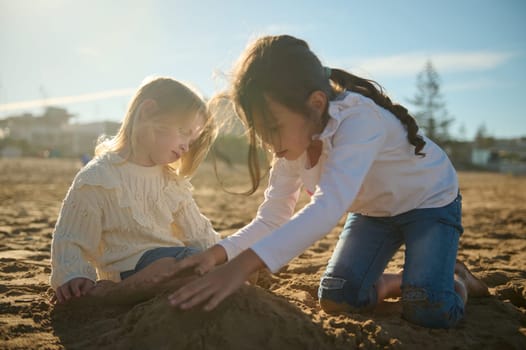 Two adorable little children girls playing together on the beach, building sandy castle on warm sunny day. People. Lifestyles, Leisure activity