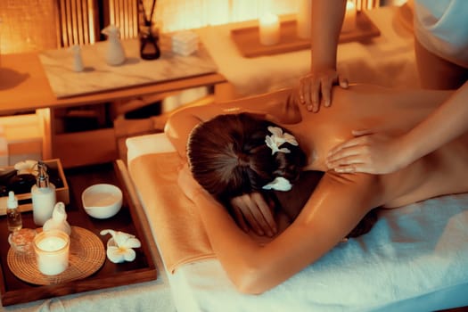 Caucasian woman customer enjoying relaxing anti-stress spa massage and pampering with beauty skin recreation leisure in warm candle lighting ambient salon spa at luxury resort or hotel. Quiescent