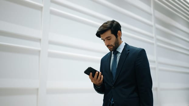 Smart manager looking at phone while standing at white background. Handsome male leader checking email or updated project and planing marketing strategy. while standing at white background. Exultant.