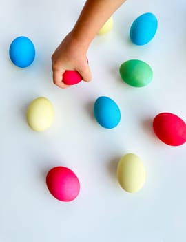 Child's hand picking up blue Easter egg among colorful eggs on white surface, interactive and engaging holiday activity concept. Can be used for educational content highlighting fine motor skills development in children, Easter egg hunt event promotions. High quality photo