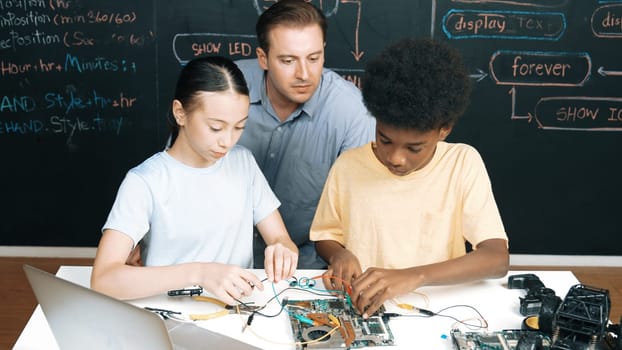 Smart mentor teach main board construction while diverse teenager learning system. Teacher explain about motherboard structure while academic student learning to use electronic equipment. Edification.