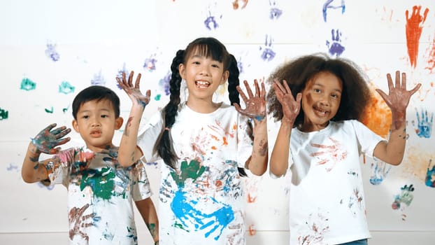 Diverse students put hands up together show colorful stained hands. Group of multicultural learner standing at white background with stained hands while looking at camera in lively mood. Erudition.