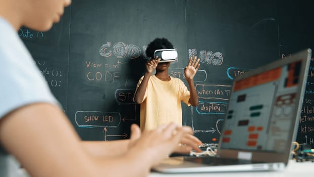 Closeup of school girl hand coding program while african student using VR interact with metaworld. Smart boy wearing virtual reality glasses and playing video games at innovative class. Edification.