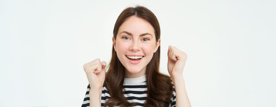 Close up portrait of cheerful woman, raising hands up and smiling, celebrating success, achievement or goal, rooting for you, looking excited at camera, white background.