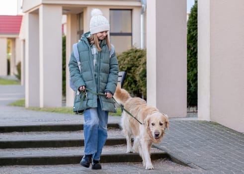 Girl In Green Jacket Walks With Golden Retriever On City Street In Early Spring