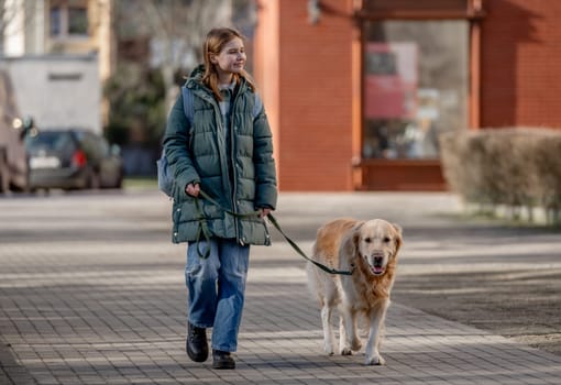 Girl In Green Jacket Walks With Golden Retriever On City Street In Early Spring