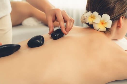 Hot stone massage at spa salon in luxury resort with day light serenity ambient, blissful couple customer enjoying spa basalt stone massage glide over body with soothing warmth. Quiescent