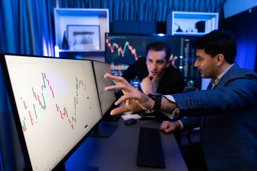 Two stock investors discussing and pointing interesting market stock on monitor. Trend of the technology for dynamic economic investment for planning to select at neon light workplace. Sellable.