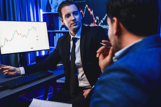 Two stock exchange traders discussing on dynamic investment graph, trending of high profit in currency stock. Showing financial benefit data on monitor screen in neon light at workplace. Sellable.