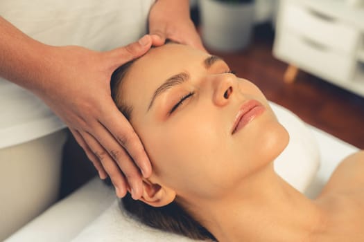 Caucasian woman enjoying relaxing anti-stress head massage and pampering facial beauty skin recreation leisure in dayspa modern light ambient at luxury resort or hotel spa salon. Quiescent