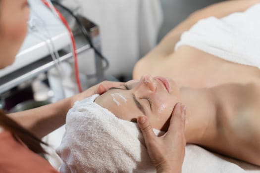 Beautiful caucasian woman lying on spa bed during having facial massage by professional hands at modern spa salon surrounded by beauty electrical equipment or medical equipment. Close up. Tranquility