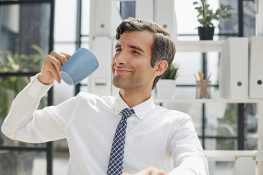 Confident businessman with coffee sitting at table in office