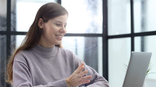 A woman in close-up at a desk in the office talking at an online video conference.