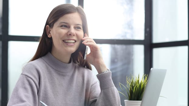 A woman in close-up at a desk in the office talking on the phone and discussing a deal.