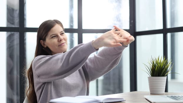 A woman in close-up at a desk in the office is warming up while working.