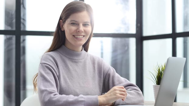 A woman in close-up at a desk in the office working and looking at the camera with a smile.