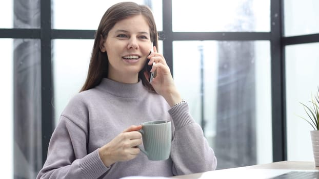 A woman in close-up talking on the phone with a cup of coffee in her hands.