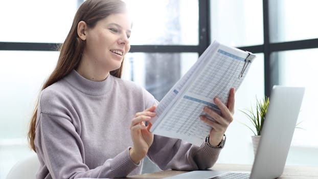 A woman in close-up at a desk in the office checks the report.