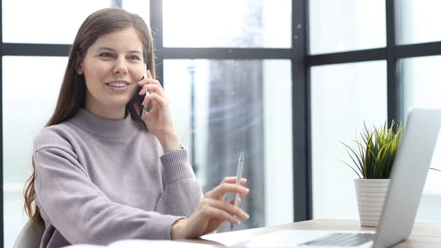 A woman in close-up at a desk in the office talking on the phone.