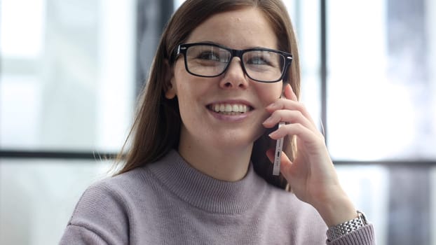 A woman with glasses in close-up in the office talking on the phone with her colleagues.