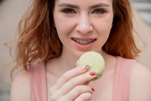 Young red-haired woman with braces eating macaron cake