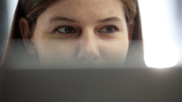 A woman's face is in close-up in the office, she is working on a laptop.