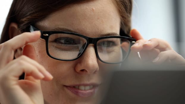 A woman's face is in close-up in the office, she is working on a laptop.