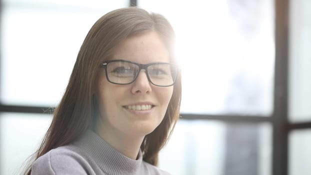 The face of a woman with glasses is a close-up in the office, she looks at the camera.