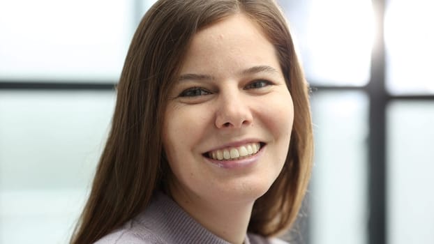 A woman's face in close-up in the office, she looks at the camera.