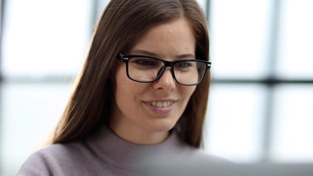 Close-up of a woman with glasses working in an office at a desk with a laptop.