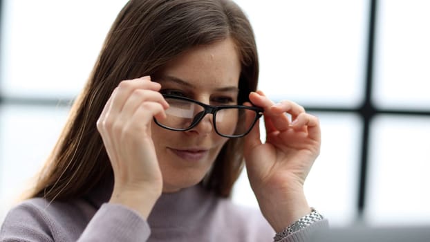 A woman with glasses in close-up working at a desk in the office on a laptop.