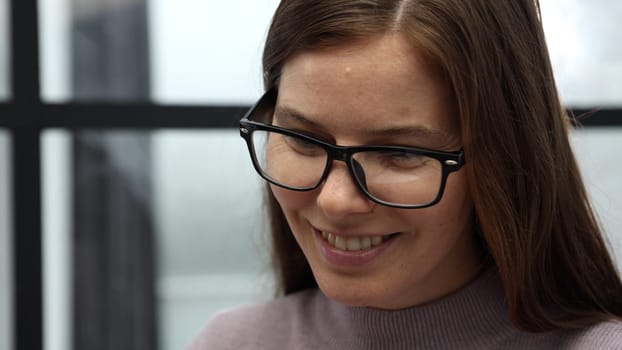 The face of a woman with glasses is a close-up in the office, she is working on a laptop.