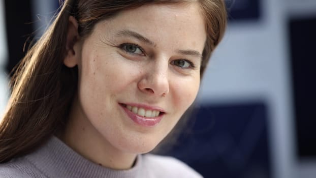 A woman's face is in close-up, she is working with charts in the office and looking at the camera.