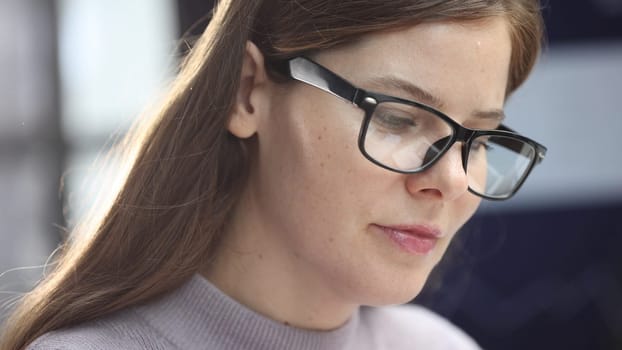 A woman's face with glasses is in close-up, she works with graphs and reports.