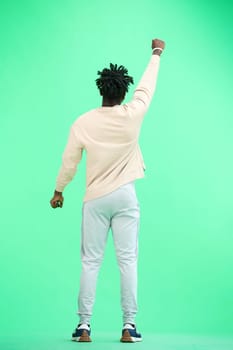 A man, full-length, on a green background, raised his hand up.