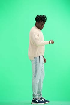 A man, full-length, on a green background, looks at his watch.