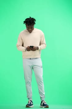 A man, full-length, on a green background, uses a phone.