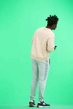 A man, full-length, on a green background, uses a phone.