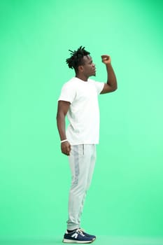 A man, full-length, on a green background, raised his hand up.