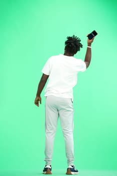 A man, full-length, on a green background, waving his phone.