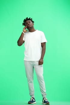 A man, full-length, on a green background, talking on the phone.