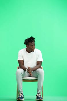 A man, on a green background, sitting on a chair.