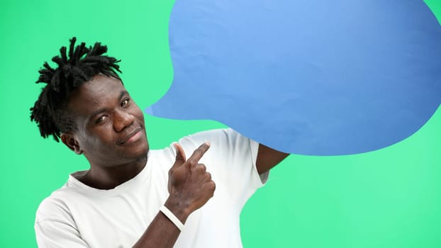 A man, close-up, on a green background, shows a blue comment sign.