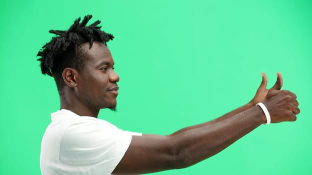 A man, close-up, on a green background, shows his thumbs up.