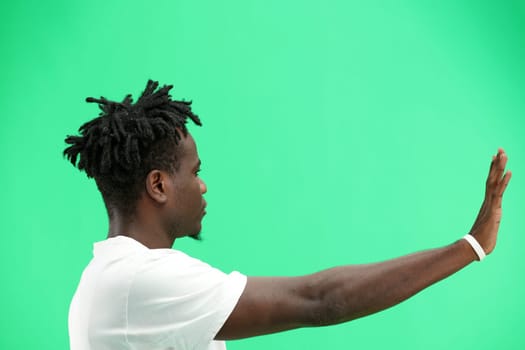A man, close-up, on a green background, shows a stop sign.