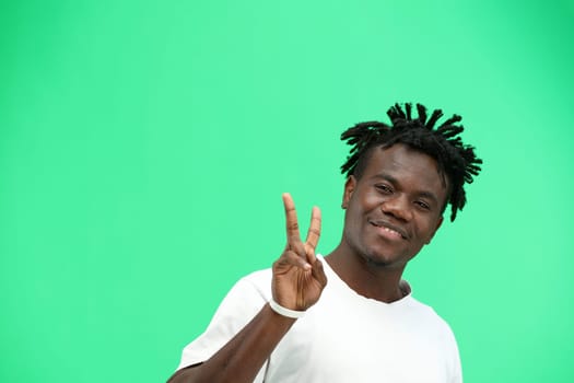 A man, close-up, on a green background, shows a victory sign.