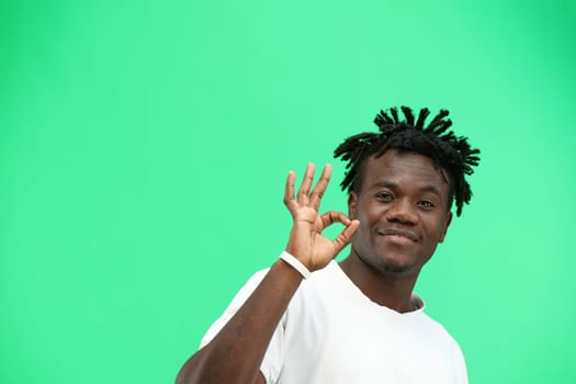 A man, close-up, on a green background, shows an ok sign.